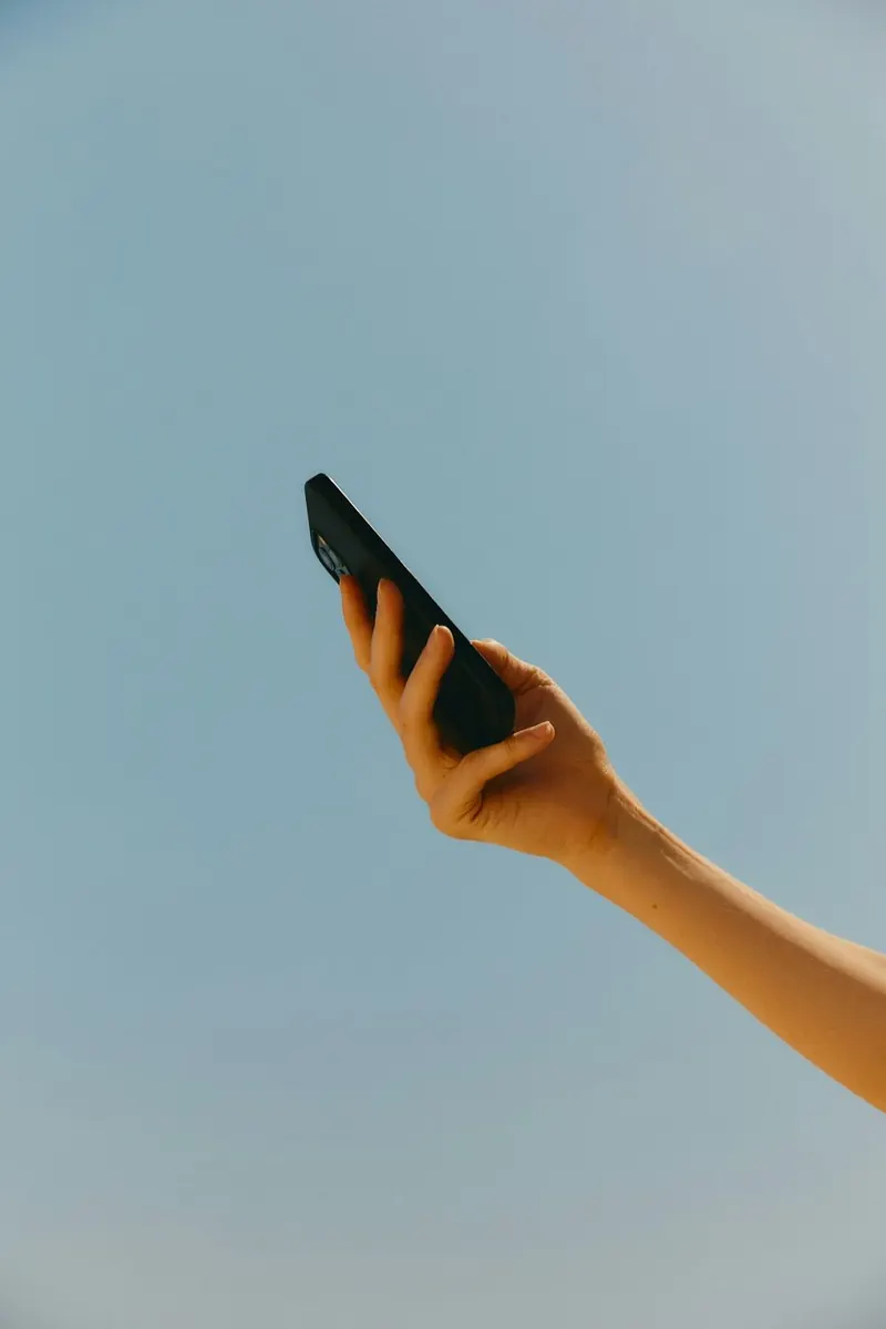 A hand holding a phone up against a blue sky