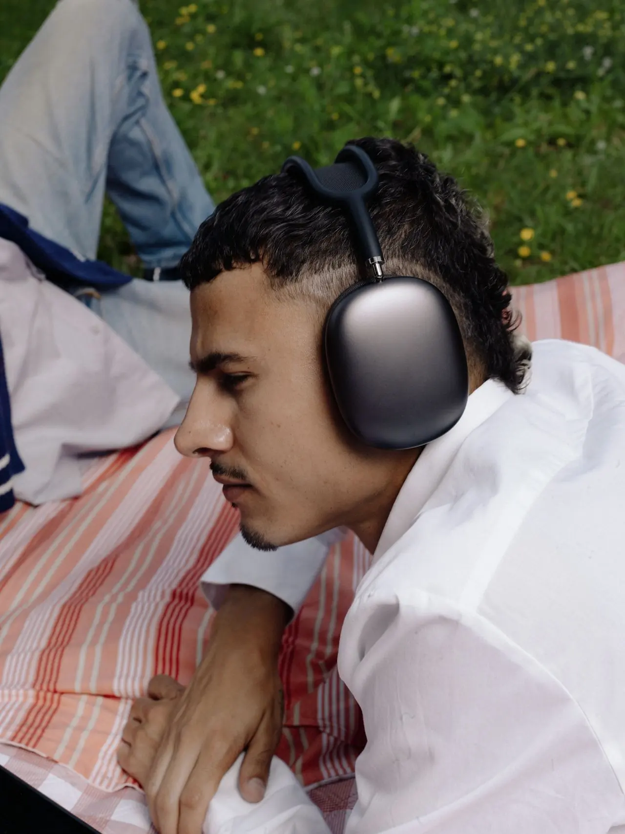 A man listening to music on headphones, lying on a picnic blanket